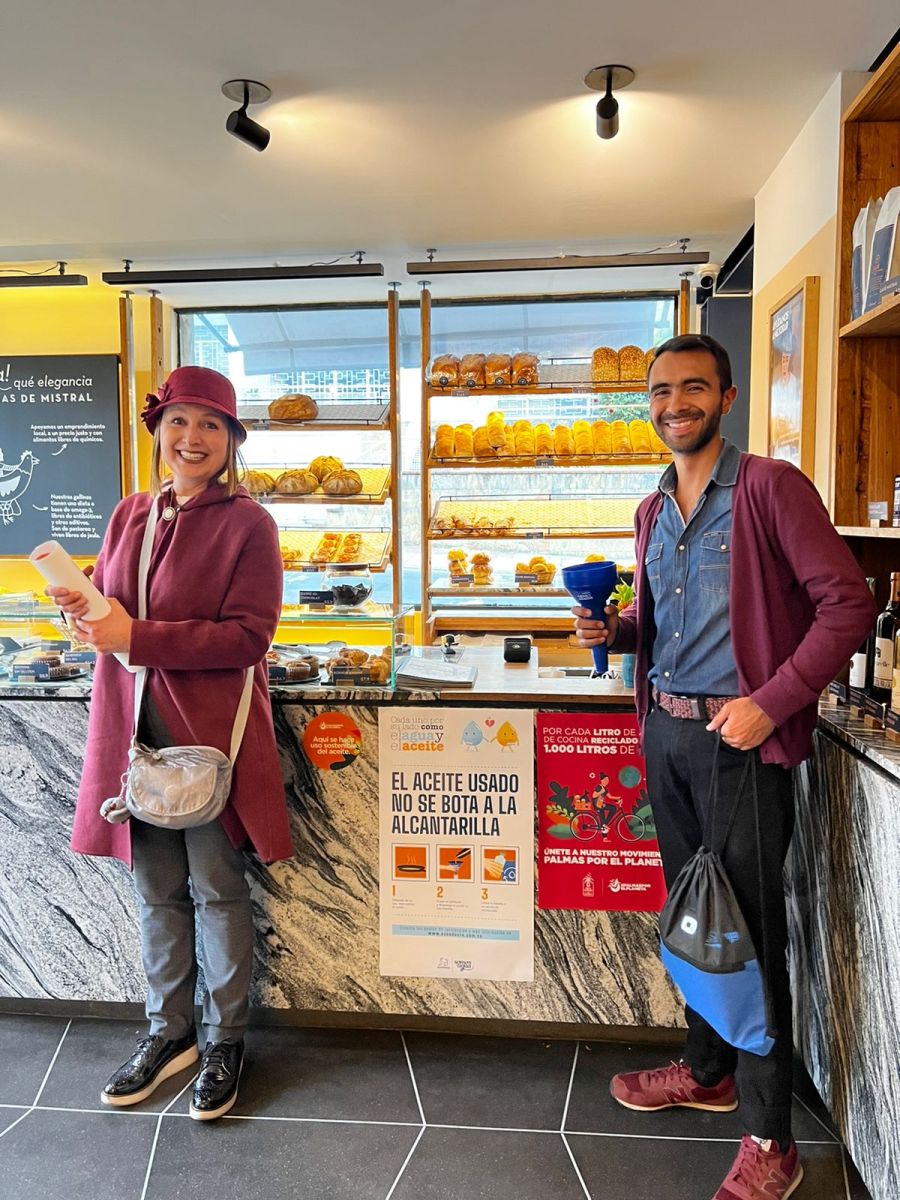 Una mujer y un hombre sonriendo, junto a carteles sobre la recolección de aceite usado.