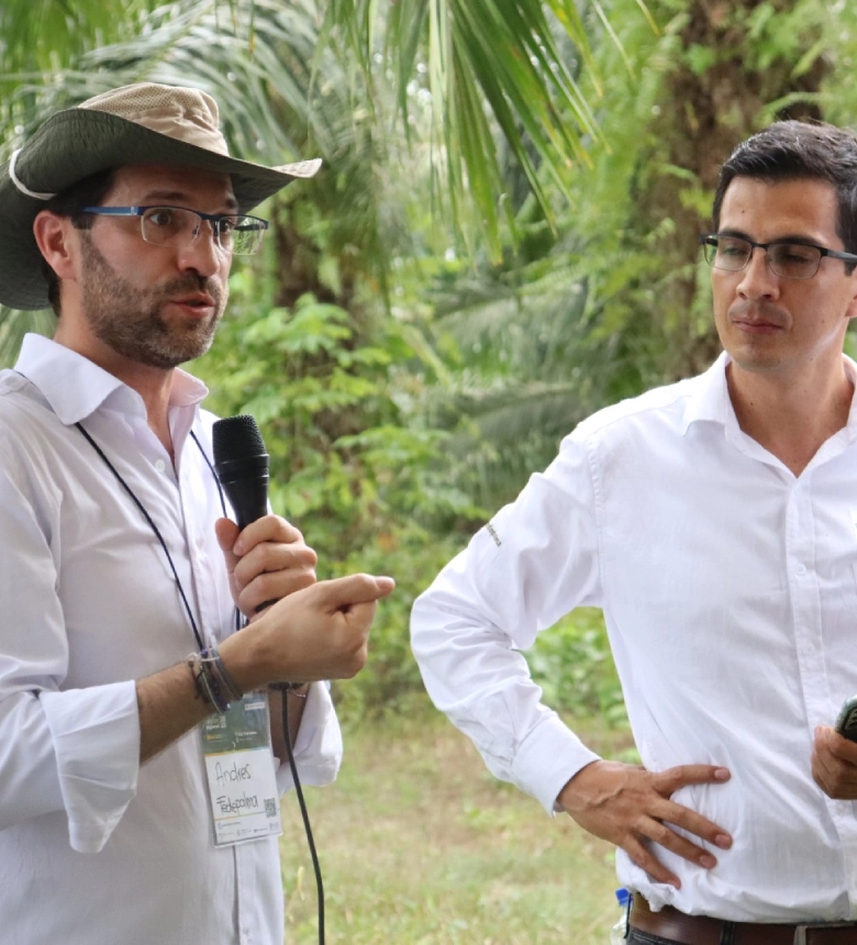 Andrés, representante de Fedepalma, dando una explicación o charla en el campo con un micrófono a otro profesional.