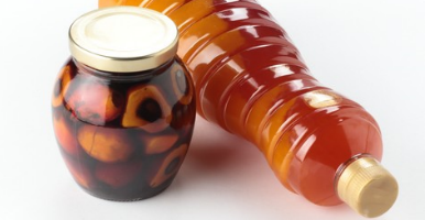 Frutos de palma de aceite conservados en un frasco de vidrio junto a una botella de aceite de palma con un líquido rojizo anaranjado.