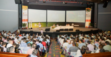 Vista general de un auditorio lleno durante una conferencia sobre la palma de aceite. Se ve el escenario con varios panelistas y pantallas grandes con el logo de 'Palma de Aceite'