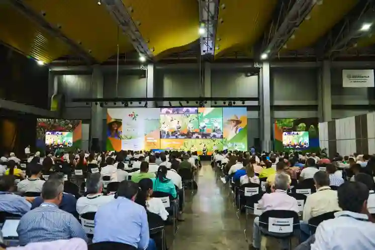 Vista amplia de un salón de conferencias con una gran audiencia sentada frente a un escenario con múltiples pantallas de presentación.