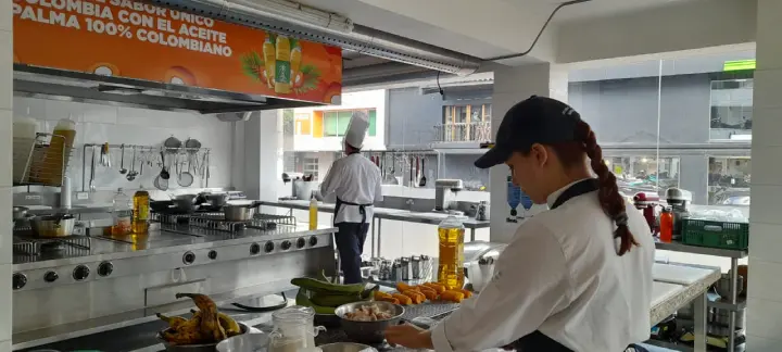 Cocinera de espaldas trabajando en una cocina industrial con anuncio de palma aceite 100% colombiano.
