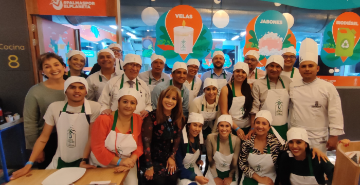 Grupo de personas con delantales y gorros de chef posando en un evento con carteles de productos de palma