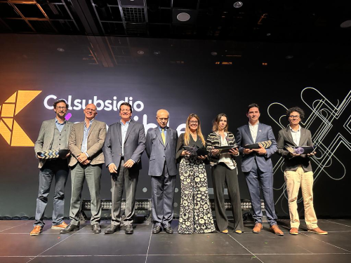 Ocho personas posando con premios en un escenario con el logo de Colsubsidio, en una ceremonia de reconocimiento.