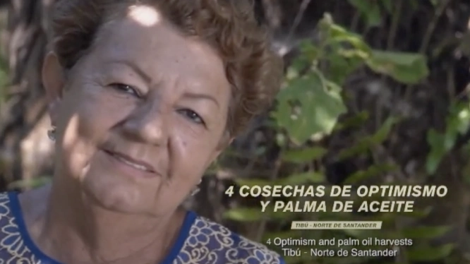 Primer plano de una mujer mayor sonriente en un entorno rural con el texto superpuesto "4 COSECHAS DE OPTIMISMO Y PALMA DE ACEITE"