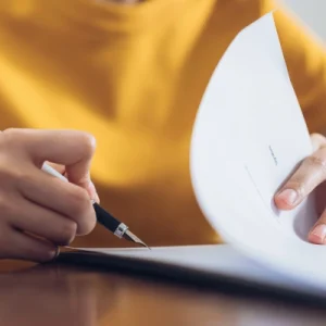 Primer plano de una persona firmando un documento con un bolígrafo.