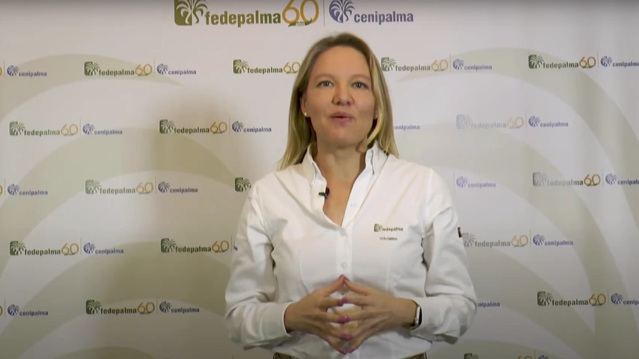 Mujer con camisa blanca, hablando frente a un fondo con los logos de Fedepalma 60 años y Cenipalma.