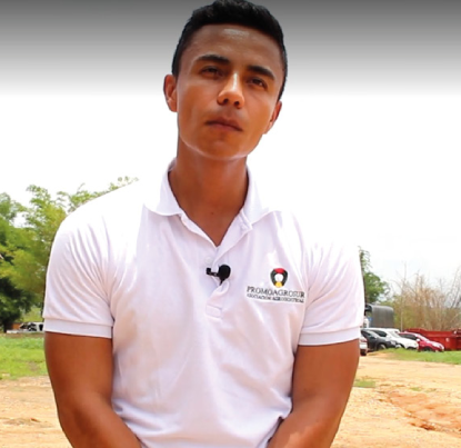 Toma media de un hombre joven de pie en un entorno rural al aire libre.