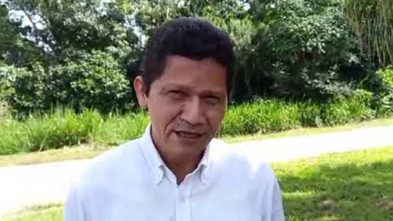 Primer plano de un hombre de pie al aire libre con fondo de vegetación verde.
