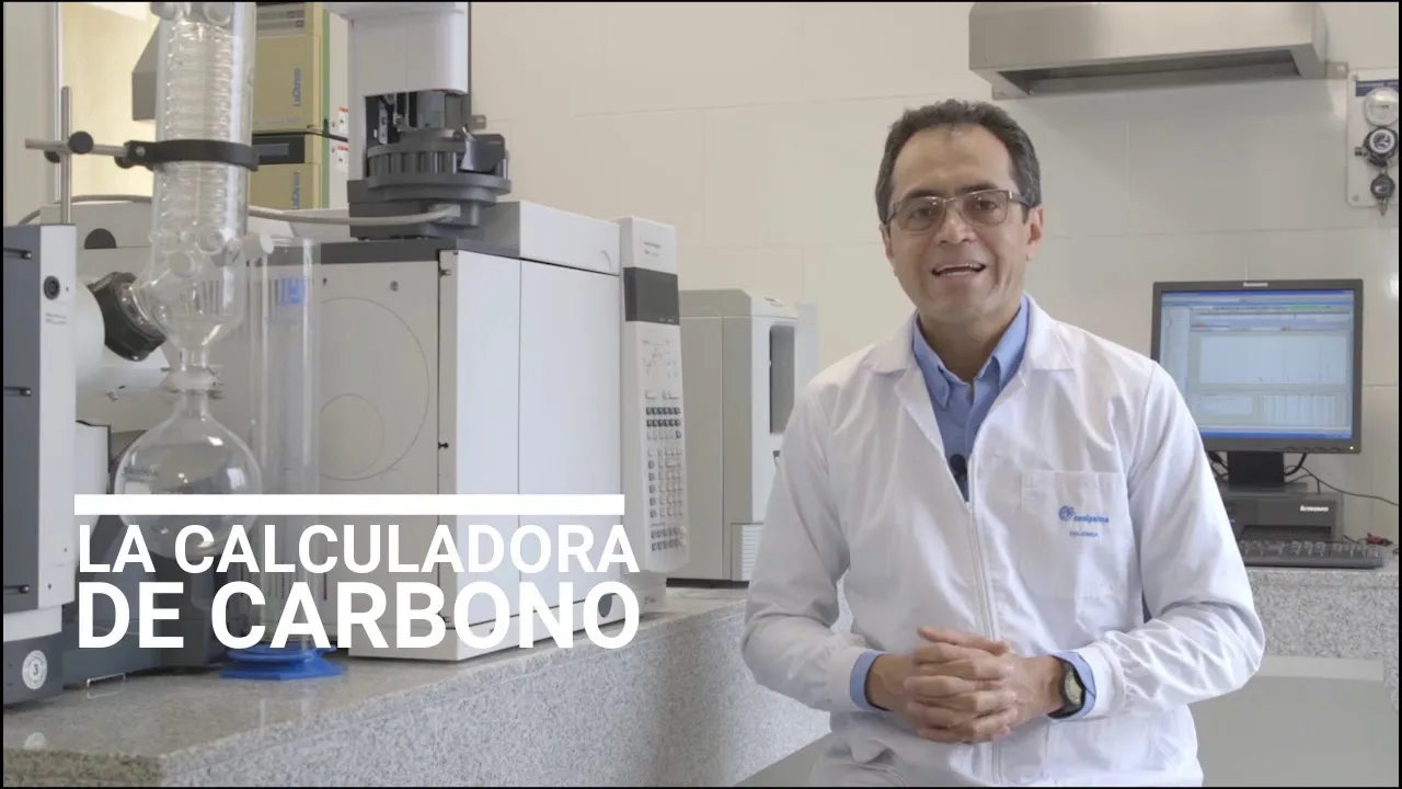 Hombre con bata de laboratorio, de pie frente a equipo científico, con el texto "LA CALCULADORA DE CARBONO"