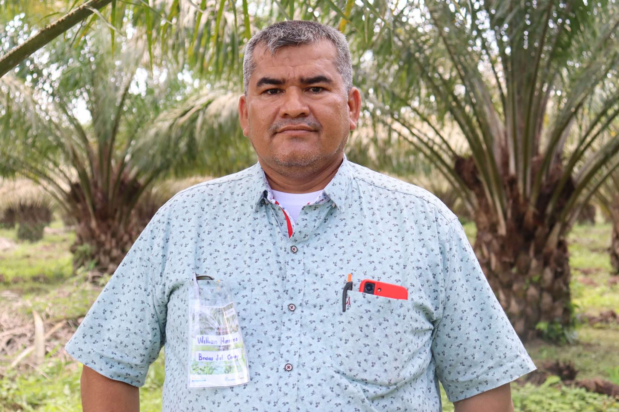 Retrato de un hombre con camisa estampada en medio de una plantación de palmeras.