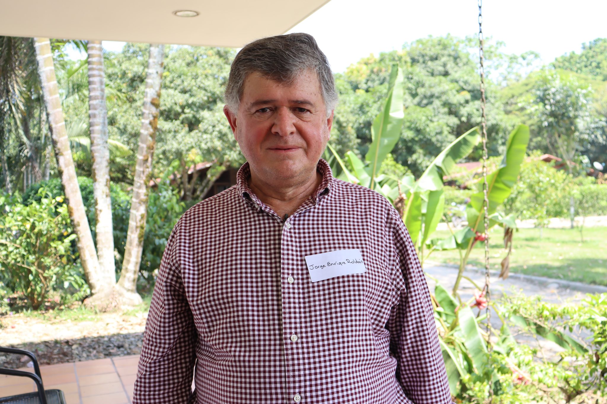 Hombre de mediana edad posando al aire libre con vegetación tropical de fondo.