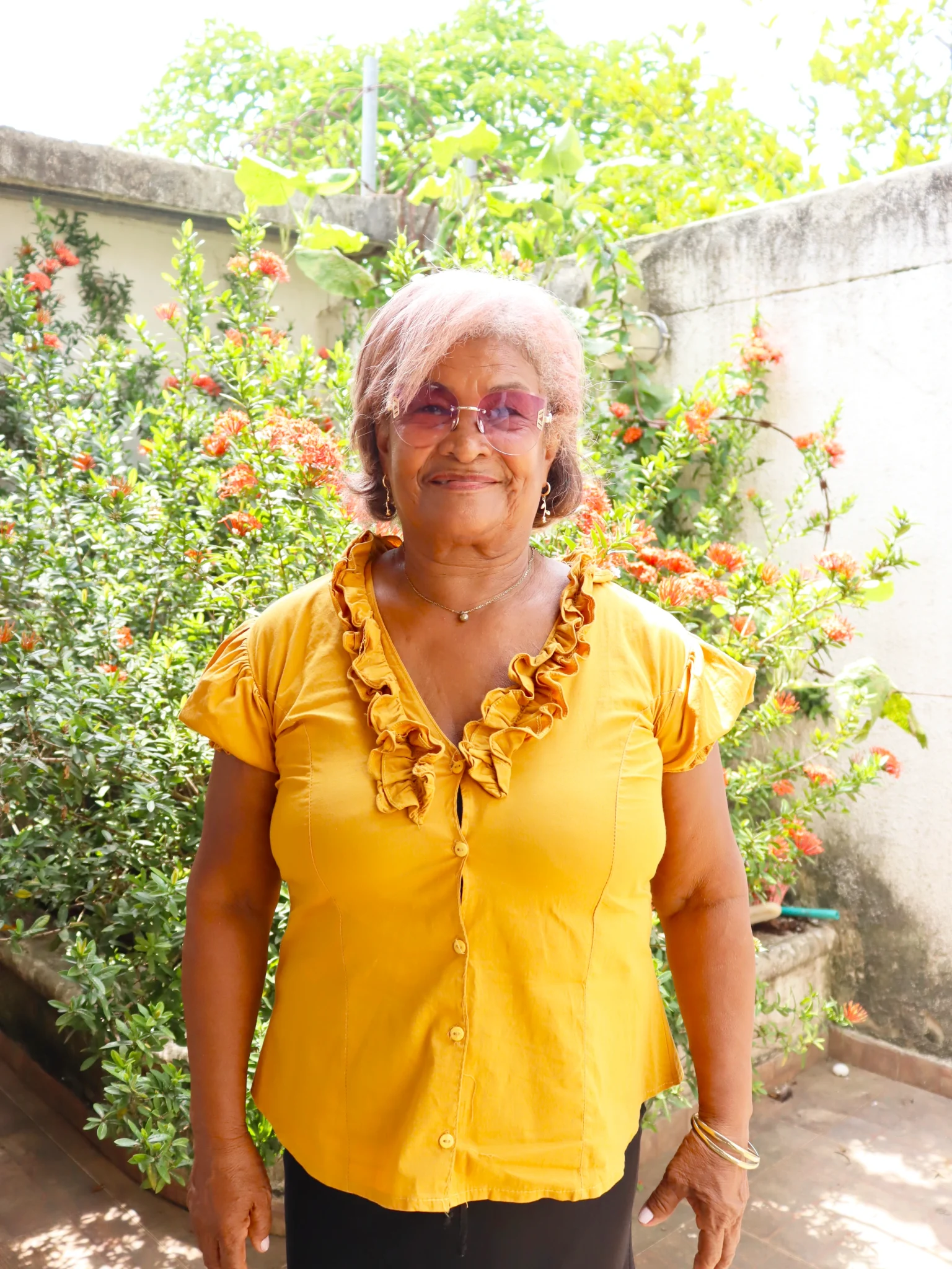 Mujer de mediana edad posando frente a una pared y arbustos con flores anaranjadas
