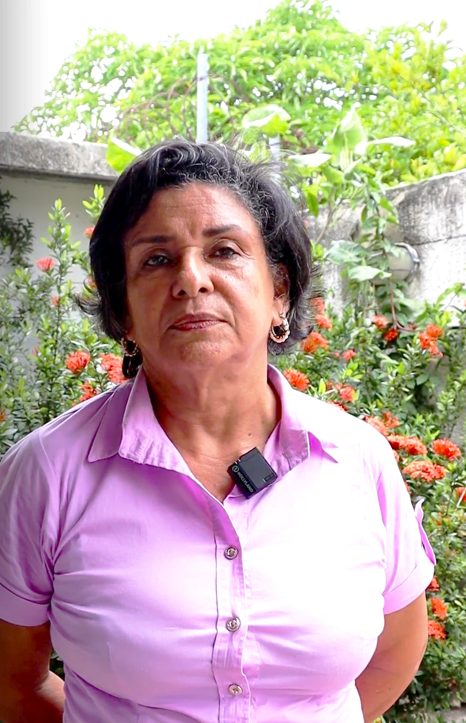 Retrato de una mujer con camisa lila, frente a un fondo de flores naranjas